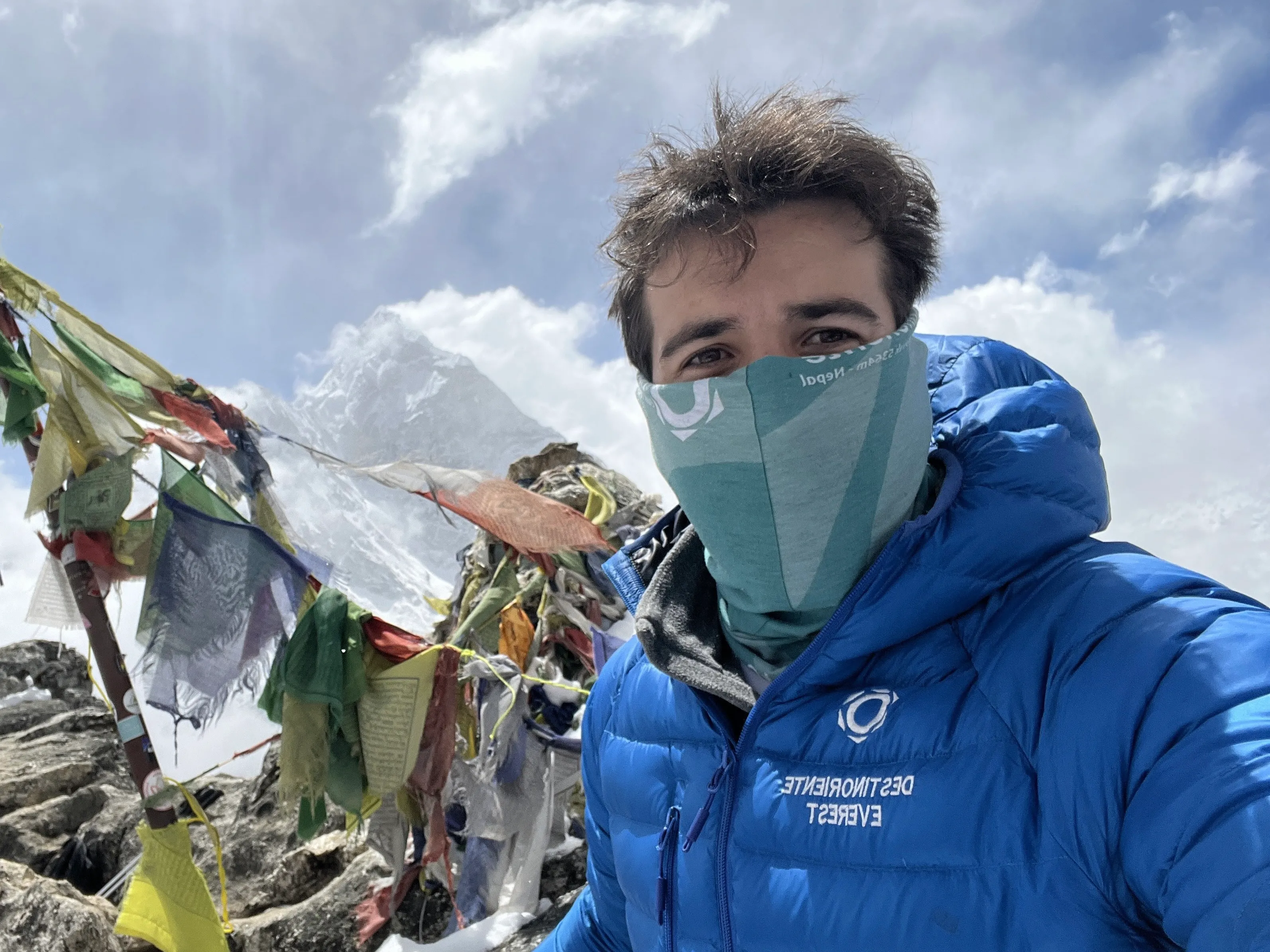 Selfie beside strings of prayer flags on a rocky summit, Ama Dablam behind the clouds